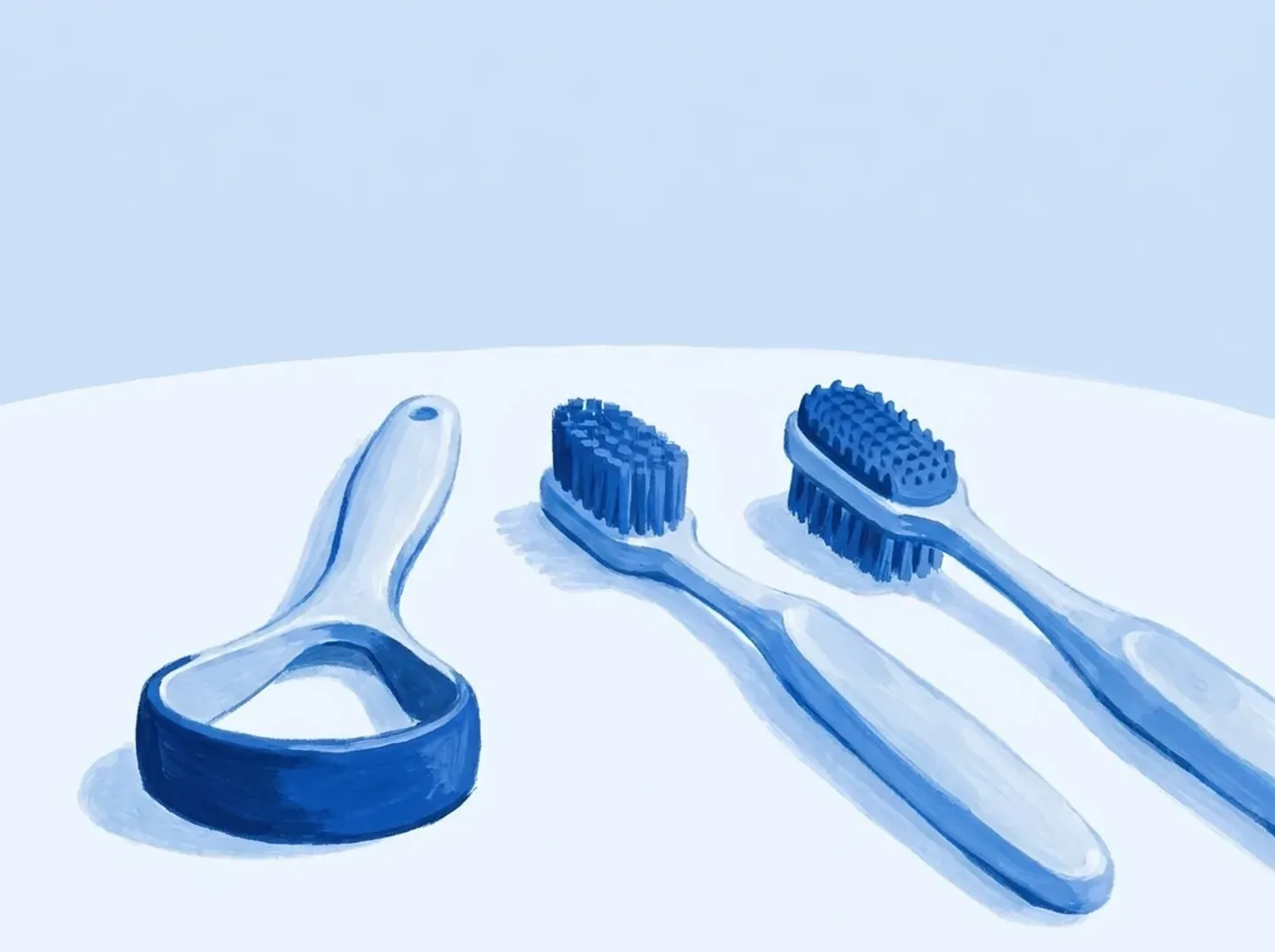 Tres utensilios alineados: un rascador de lengua, un cepillo normal y un cepillo con el dorso de goma