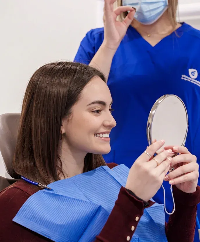 Una paciente se mira la sonrisa en un espejo de mano en la consulta