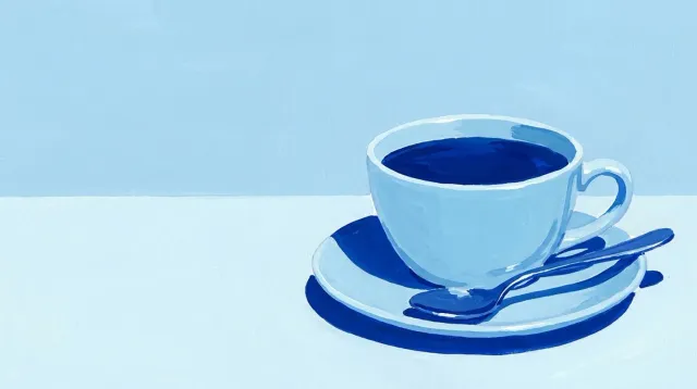Una cuchara de metal apoyada en el borde de una taza, sobre la mesa