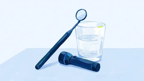 Un espejo dental y una pequeña linterna sobre una mesa, junto a un vaso de agua.